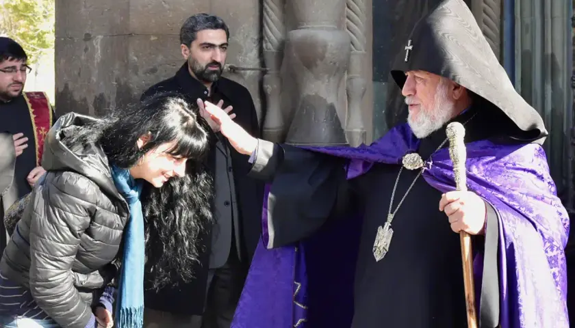 Błogosławieństwo kobiety przez duchownego w tradycyjnym ornamencie. Scena ukazuje głębokie korzenie armenia religia.