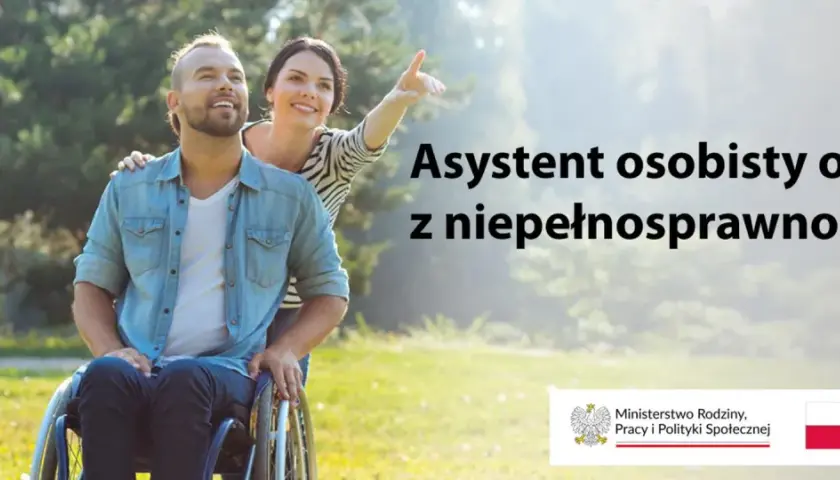 Uśmiechnięty mężczyzna na wózku inwalidzkim i kobieta wskazująca palcem w dal. Asystent osoby z niepełnosprawnością 2026.