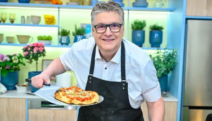 Uśmiechnięty kucharz prezentuje pyszną pizzę rzymską prosto z pieca.