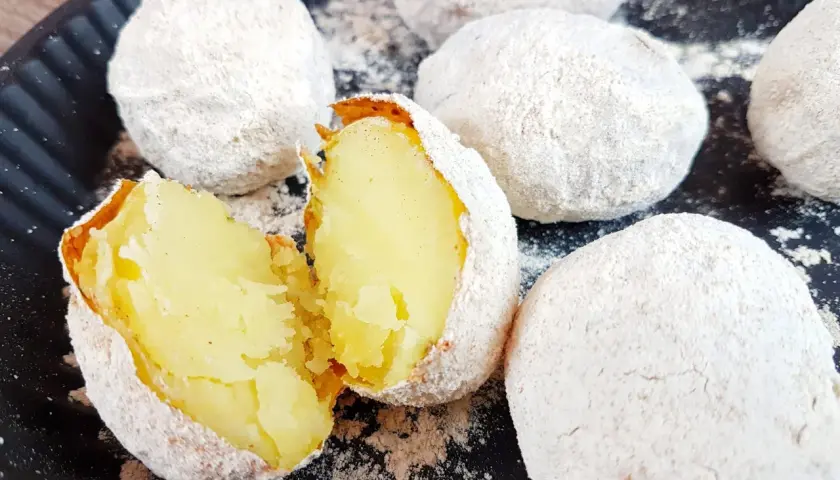 Pyszne ziemniaki z ogniska, upieczone w popiele, jeden przekrojony na pół, ukazujący miękki, żółty środek.