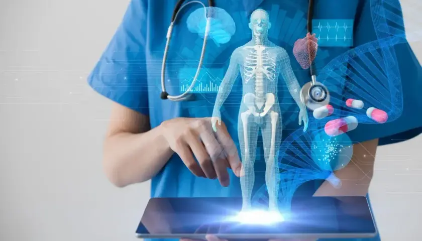 Lekarz w niebieskim fartuchu trzyma tablet z hologramem ludzkiego ciała, organów i DNA.