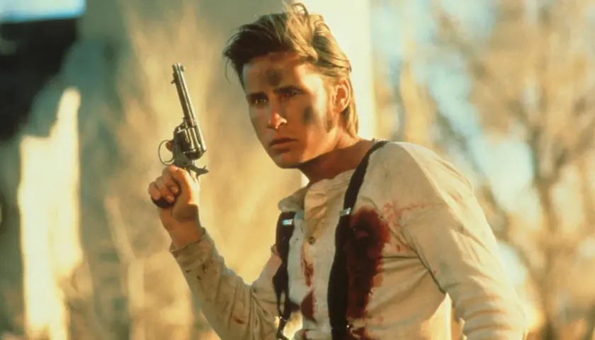 En ung man med smuts i ansiktet och blodfläckar på skjortan håller en revolver. Han är en del av rollistan i Young Guns.