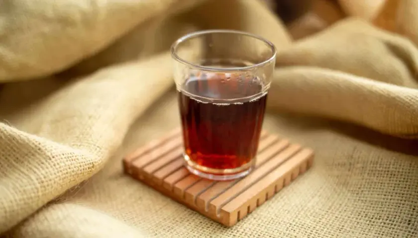 Ein Glas roter Rooibos Tee, perfekt für die Stillzeit, steht auf einem Holzuntersetzer.
