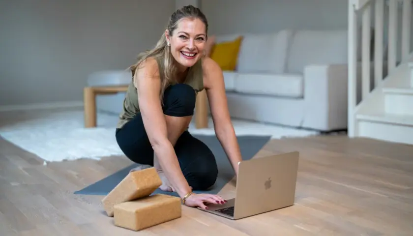 Glad kvinna förbereder sig för en lugn yogaövning med hjälp av en laptop och **restorative yoga positioner**.