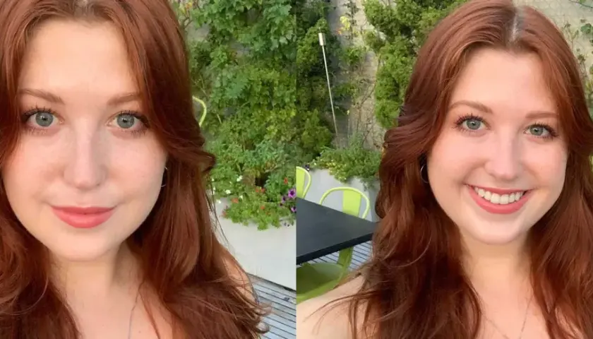 Mujer con cabello largo y ondulado en tonos tinte pelirrojo, ojos azules y pecas, sonríe en un entorno exterior con vegetación.