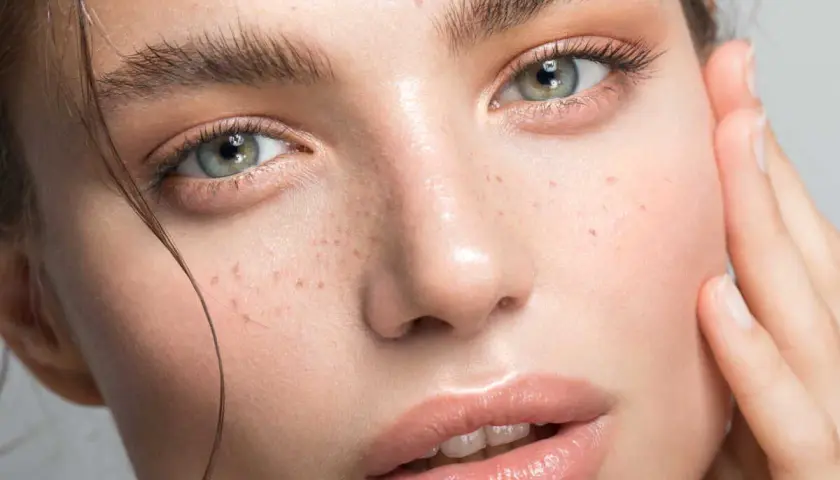 Un visage de femme aux yeux verts et aux taches de rousseur. La poudre libre matifie et fixe le maquillage pour un teint parfait.