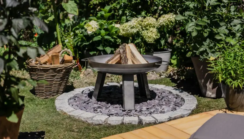 Schöne Feuerstelle im Garten mit Holzkorb und Pflanzen. Tolle Feuerstelle Garten Ideen für gemütliche Abende.