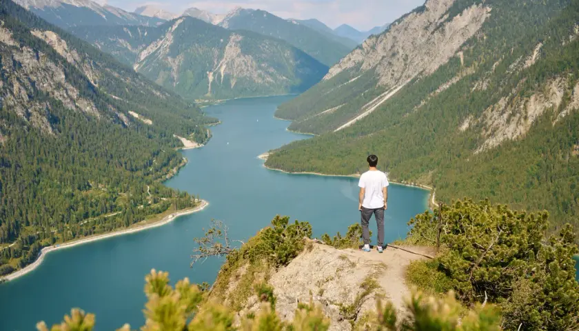 Mann genießt atemberaubende Aussicht beim Plansee Wandern. Türkisblaues Wasser, grüne Wälder und majestätische Berge.