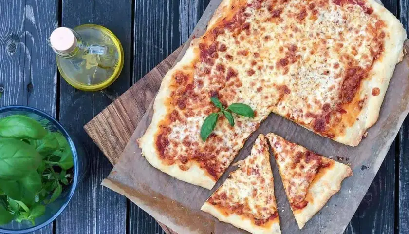 Pyszna pizza margherita z roztopionym serem i świeżą bazylią, obok buteleczka oliwy i miseczka z ziołami.