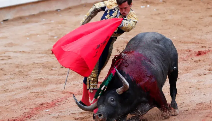 Un torero con traje de luces se enfrenta a un toro ensangrentado, evocando el origen de la tauromaquia.