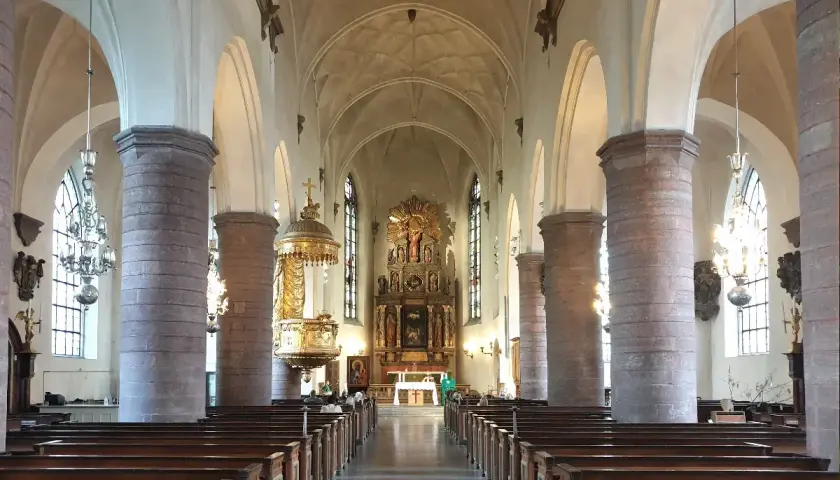 Interiör av St Jacobs kyrka med bänkar, pelare och altare.