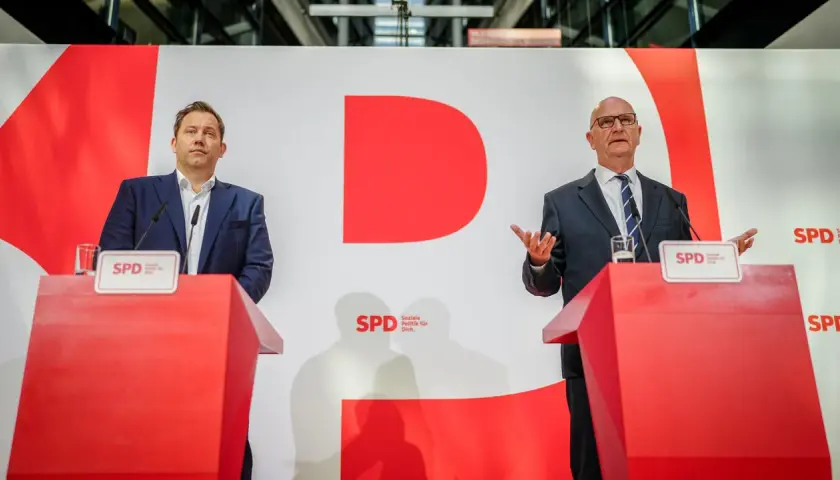 Zwei Männer stehen an roten Rednerpulten vor einer großen roten "D"-Grafik. Sie sprechen über das wahlergebnis brandenburg.