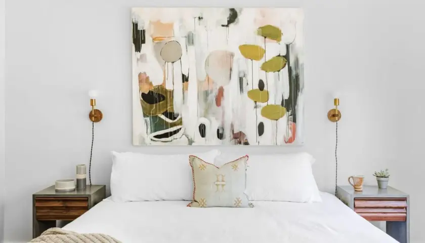 Staging a master bedroom with a large abstract painting above a white bed, flanked by modern nightstands and sconces.
