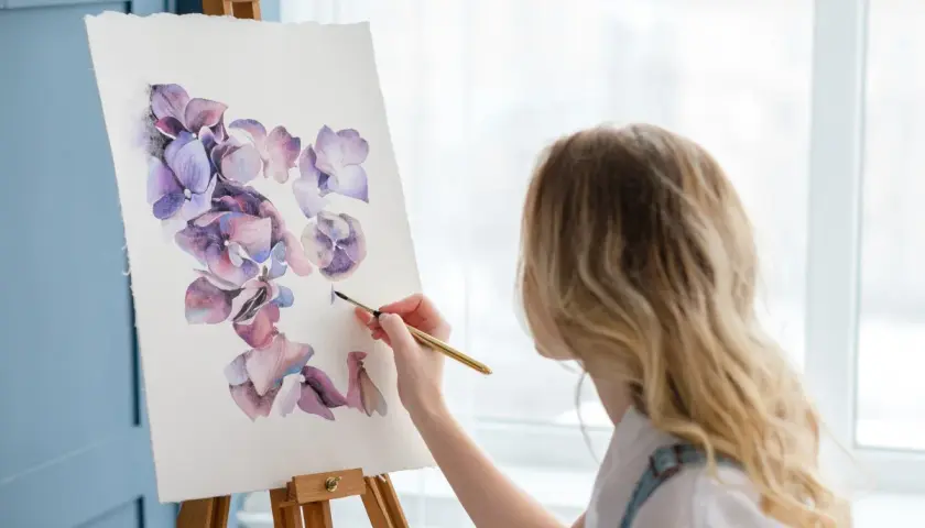 Kobieta maluje akwarelami fioletowe kwiaty. To inspiracja, jak być kreatywnym, tworząc piękno.