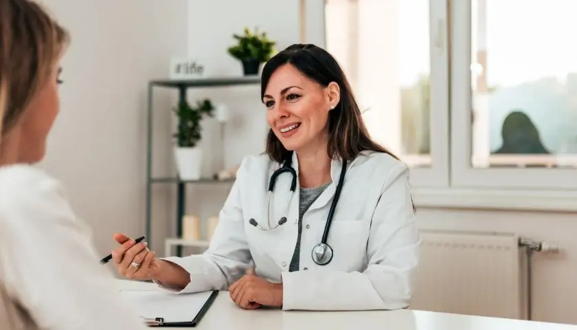 Medico sorridente parla con paziente, illustrando un punto con la penna. La scena evidenzia una buona comunicazione medico-paziente.