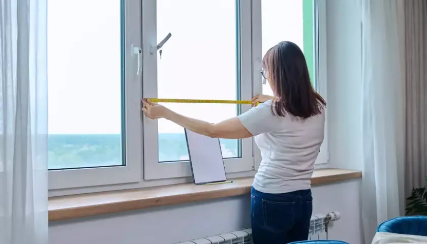 Une femme mesure une fenêtre, pensant à l'avantage d'un achat immobilier neuf pour personnaliser son espace.