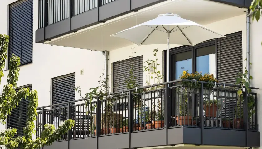 Nowoczesny balkon w bloku z roślinami w doniczkach i białym parasolem. Inspiracja, jak wykończyć balkon w bloku, by był funkcjonalny i estetyczny.