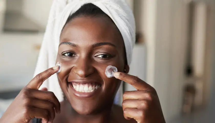 Sonrisa radiante de mujer con toalla en la cabeza, aplicándose crema. Un vistazo al **retinol antes y después** para una piel luminosa.