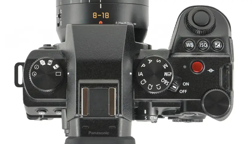 Górna część aparatu Panasonic Lumix G9 II z obiektywem 8-18 mm. Widoczne pokrętła trybów, przyciski i ekran.