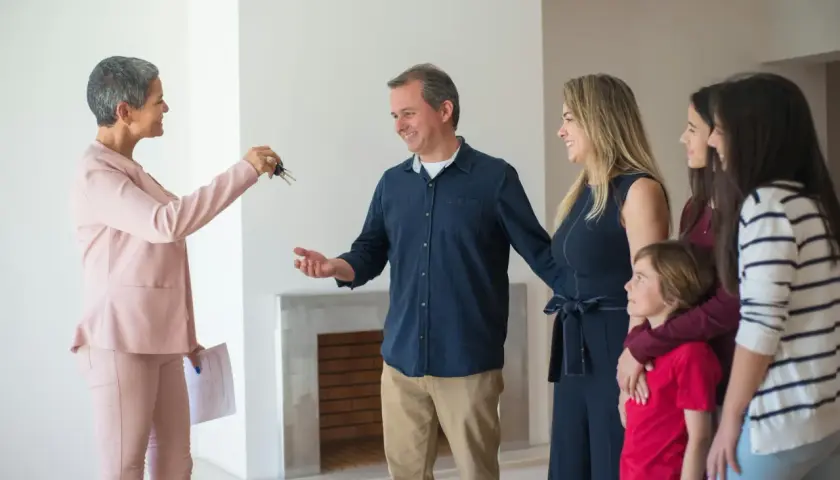 Rodzina odbiera klucze do nowego domu. Agentka nieruchomości przekazuje je, a rodzice z dziećmi patrzą z radością. To symboliczny moment, jak zadatek na przyszłość.