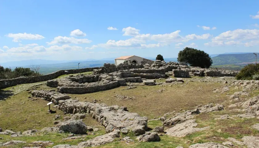 Rovine del santuario nuragico di Santa Vittoria sotto un cielo azzurro con nuvole bianche.