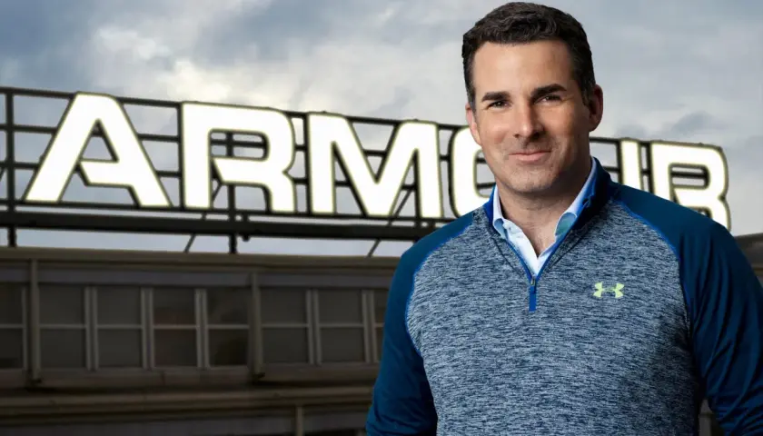 Mężczyzna w bluzie Under Armour na tle budynku z napisem ARMOUR.