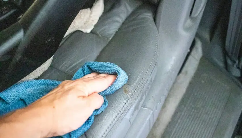 Ręka z niebieską ściereczką czyści skórzane fotele samochodowe.
