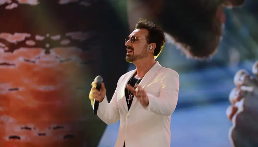 Mateusz Ziółko w białej marynarce śpiewa do mikrofonu na scenie.