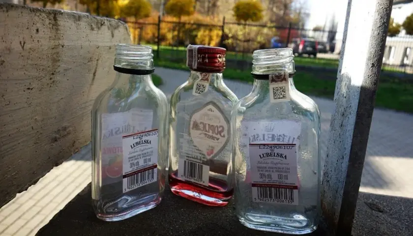 Trzy puste butelki po alkoholu, w tym jedna z czerwonym płynem, leżą na betonowym murku. Małpka alkoholowa, symbol beztroski, ale i problemu.