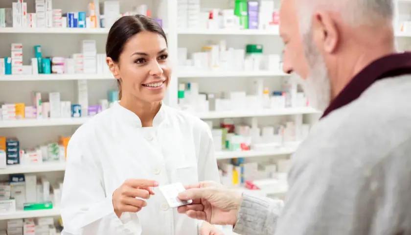 Farmaceutka podaje starszemu panu opakowanie leku, sugerując eliquis zamiennik.