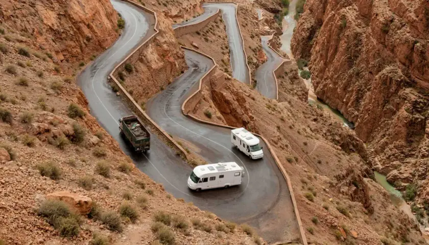 Deux camping-cars naviguent sur une route sinueuse à flanc de montagne au Maroc, traversant un paysage désertique spectaculaire.