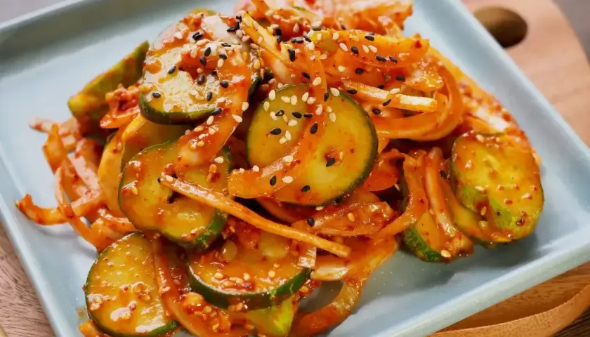 Pikantne ogórki po koreańsku z cebulą i sezamem, podane na jasnoniebieskim talerzu.