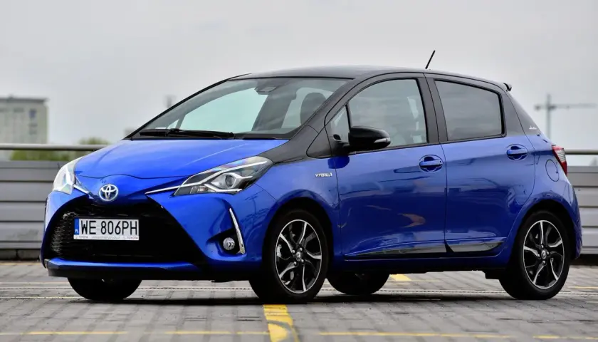 Niebieska Toyota Yaris Hybrid, z czarnym dachem, zaparkowana na zewnątrz. Ile koni ma Toyota Yaris? Ten model ma 100 KM.