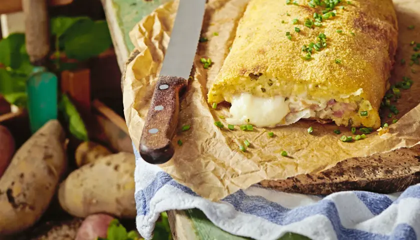 Herzhaft gefüllte polpette di patate, goldbraun paniert, mit geschmolzenem Käse im Inneren. Frische Kartoffeln liegen daneben.