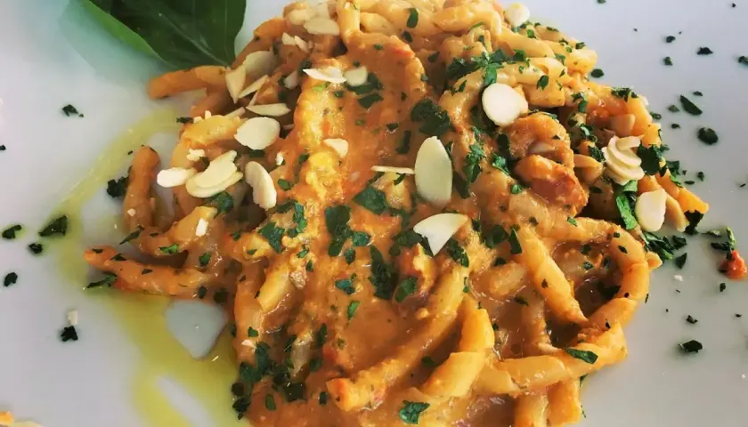 Busiate alla trapanese, un piatto di pasta siciliana con un sugo ricco, guarnito con mandorle a lamelle e prezzemolo fresco.