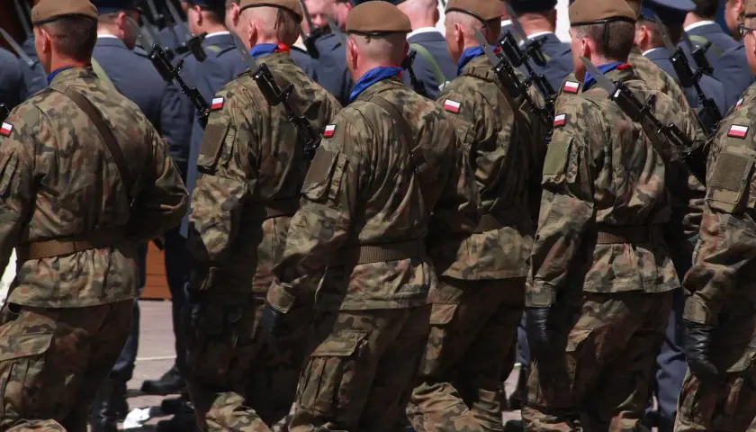 Żołnierze w mundurach polowych maszerują w szyku, każdy z bagnetem na karabinie.