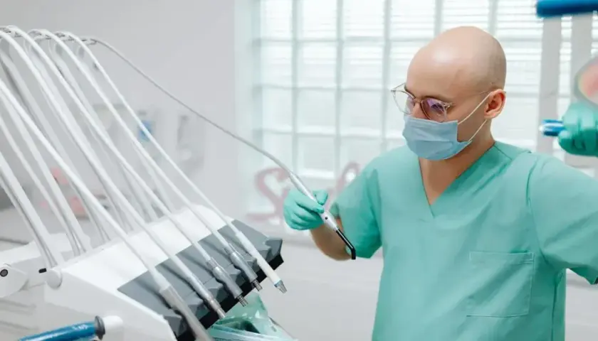 Dentysta w masce i okularach trzymający narzędzie przy unitu stomatologicznego.