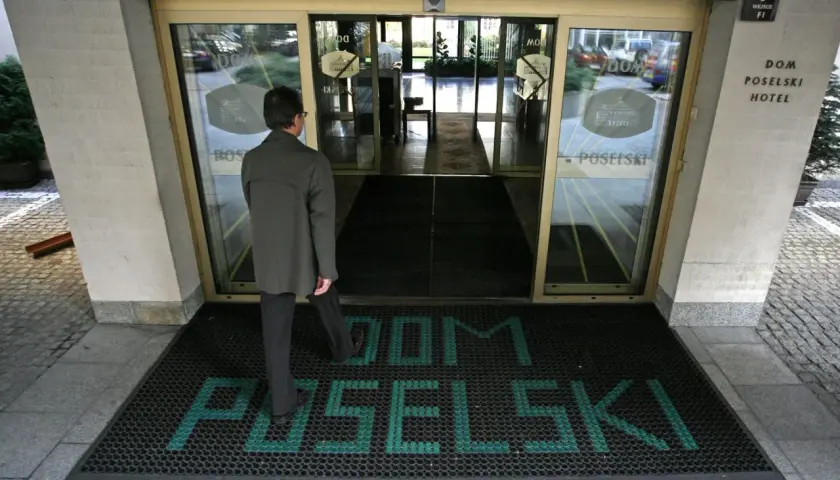 Mężczyzna wchodzi do hotelu poselskiego. Na wycieraczce przed wejściem widnieje napis "DOM POSELŚKI".