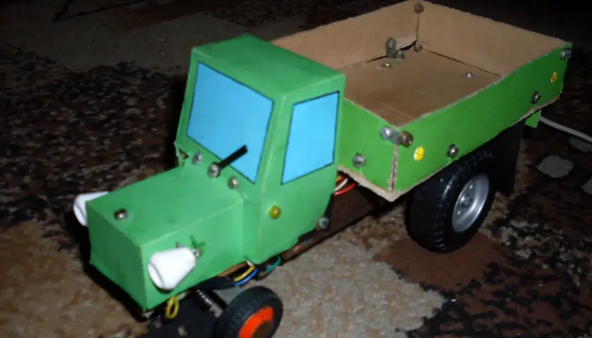 Zielony traktor z kartonu, z niebieskimi szybami i drewnianą skrzynią. Oto jak zrobić taki traktor z kartonu!