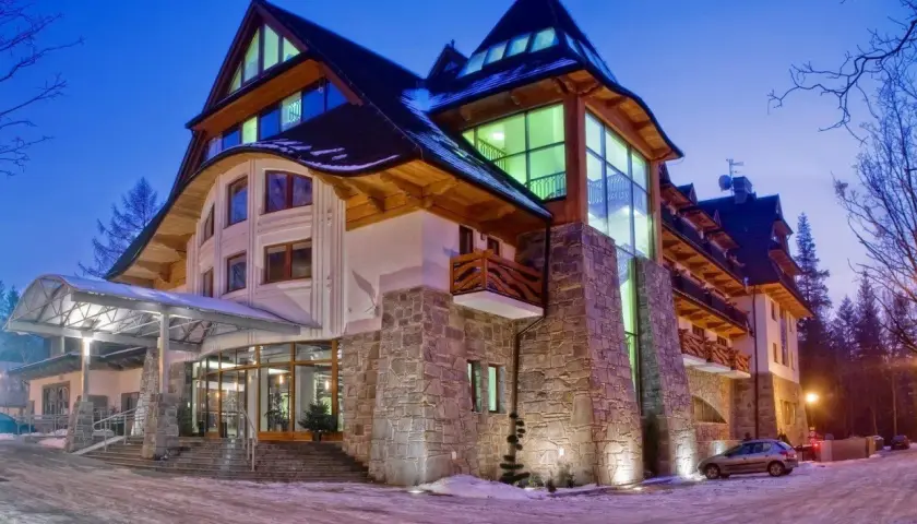 Elegancki hotel Crocus w zimowej scenerii, z kamienną fasadą i drewnianymi elementami, oświetlony nocą.