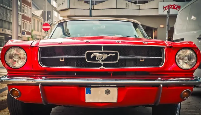 Czerwony Ford Mustang z lat 60. z emblematem galopującego konia na grillu.