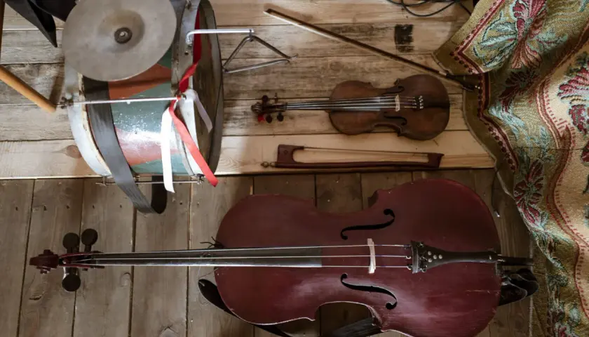 Instrument ludowy podobny do wiolonczeli, skrzypce i bębenek leżą na drewnianej podłodze.