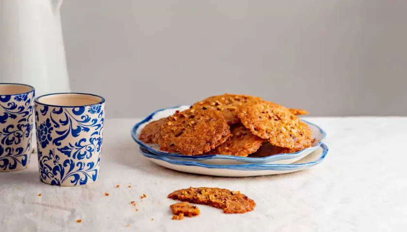 Deliciosas galletas de jengibre crujientes con trozos de nueces, servidas en un plato azul y blanco.