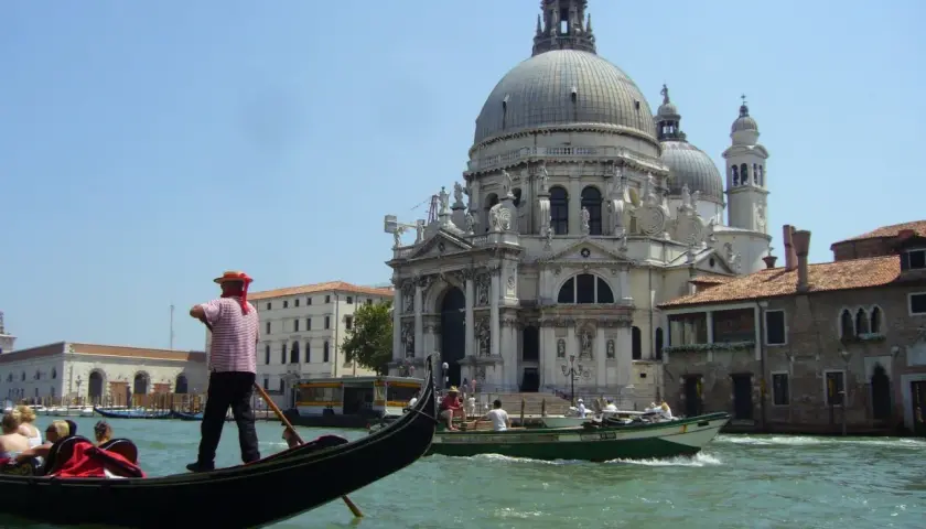 Gondolier wita turystów w Wenecji. W tle Bazylika Santa Maria della Salute i kanał.