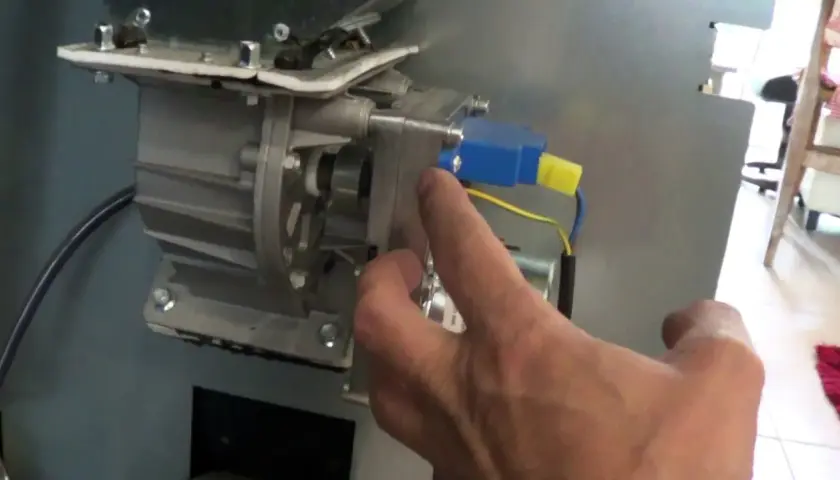 Main d'un homme manipulant le mécanisme d'un poêle à granulés, pour nettoyer le pressostat.