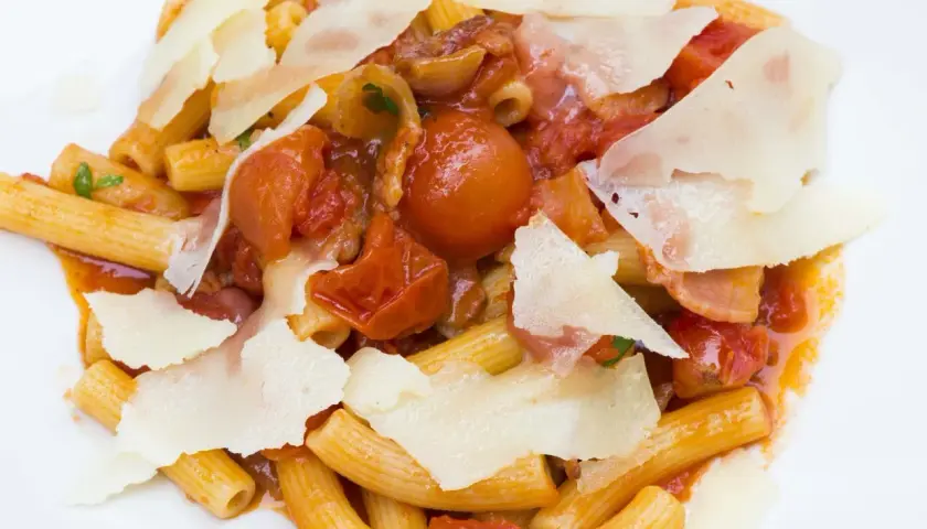 Piatto di rigatoni conditi con un ricco sugo amatriciana, pomodorini, guanciale e scaglie di pecorino.