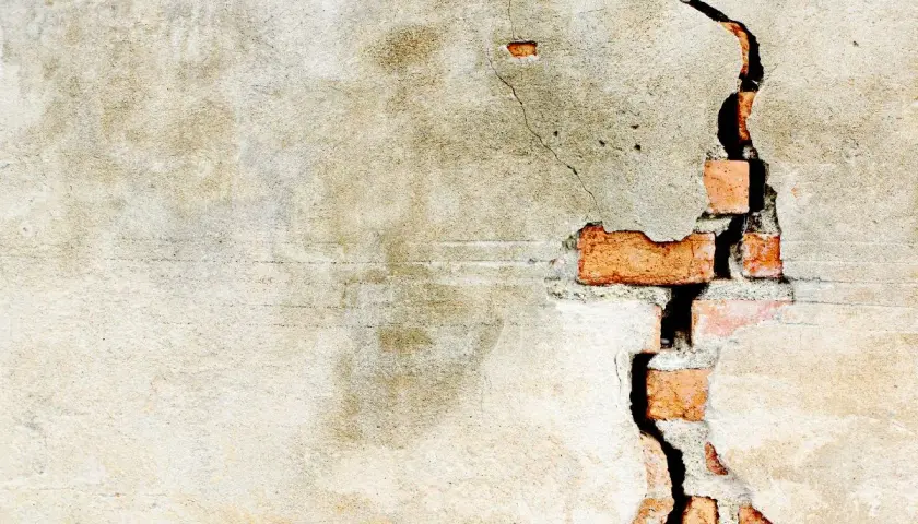Crepe intonaco interno rivela mattoni rossi. La parete mostra segni del tempo e usura.