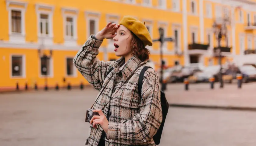 Dziewczyna w żółtym beracie i kratowej kurtce z aparatem szuka inspiracji na ciekawe tematy do rozmowy z dziewczyną.