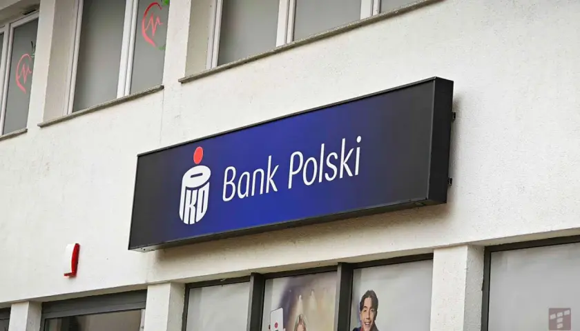 Logo Banku Polskiego na niebieskim tle. Obok widoczny czerwony sygnalizator. W tle okna z grafikami, być może ankieta AML.