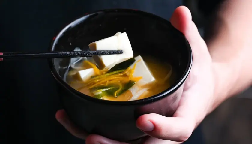 A chopstick lifts a cube of tofu from a bowl of miso soup, showcasing simple yet delicious tofu recipes.